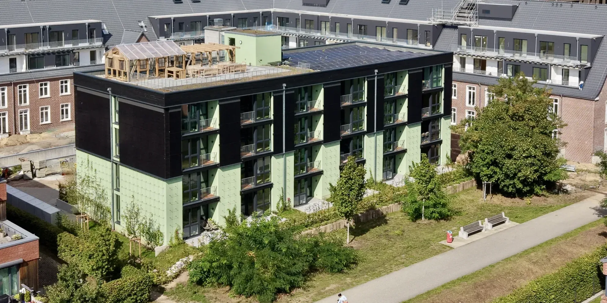 Smoodje aus erhöhter Schrägperspektive mit grün-schwarzer Fassade, Dachterrasse und Gewächshauskonstruktion. | Seniorenresidenz Fischbeker Höfe